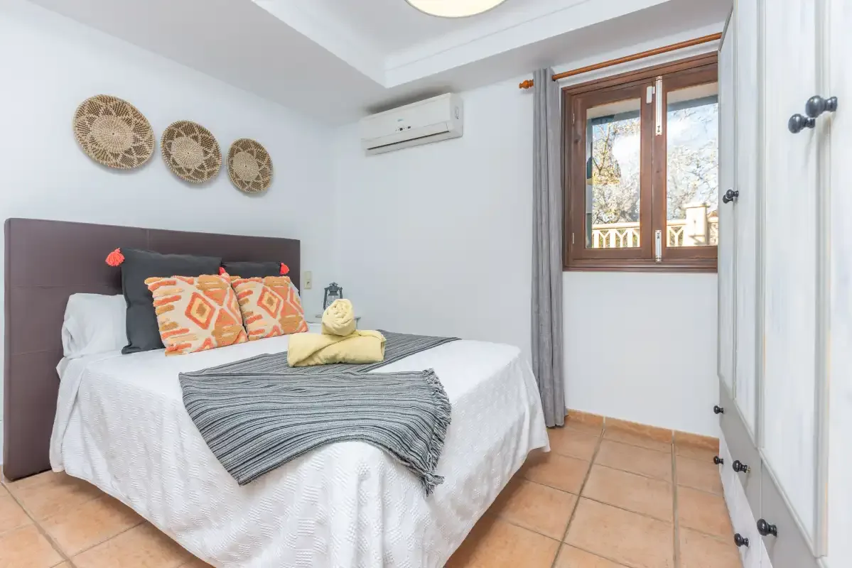 Un dormitorio con una cama, cojines estampados y una ventana.