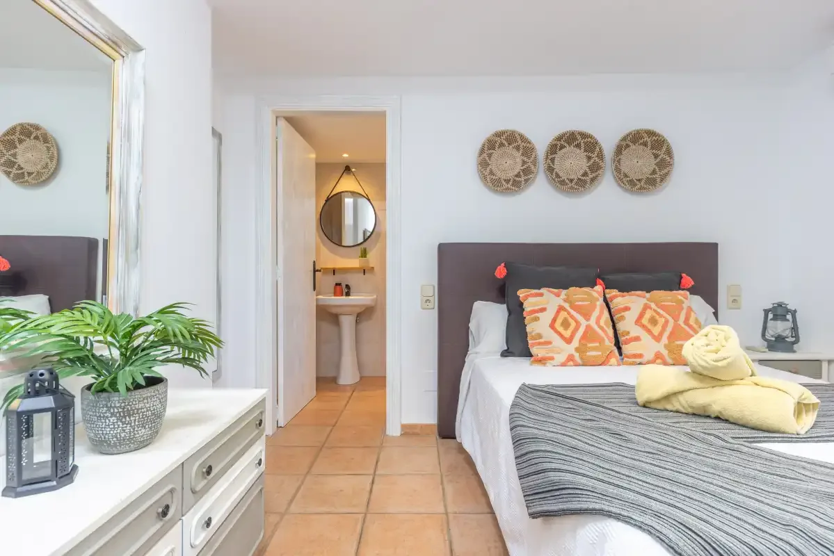 Un dormitorio con una cama bien tendida y un tocador junto a la puerta.