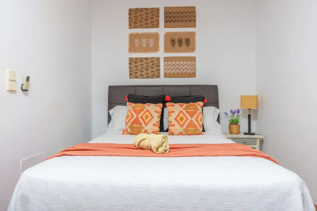 Un dormitorio ordenado con una cama, cojines estampados y cuadros en la pared.