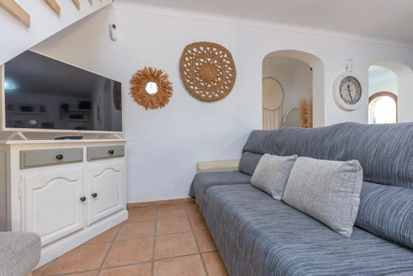 Una sala de estar con un sofá gris, un televisor y adornos tejidos en la pared.