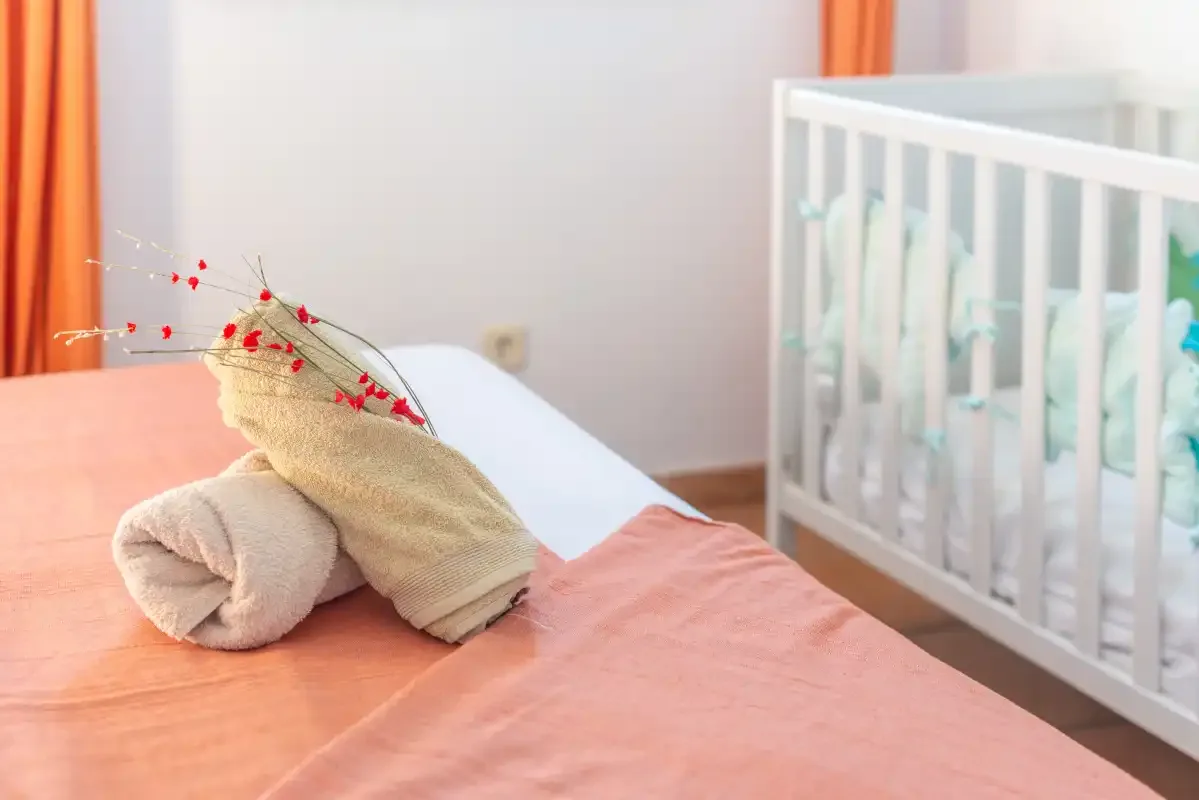 Un dormitorio con toallas dobladas sobre una cama junto a una cuna blanca.