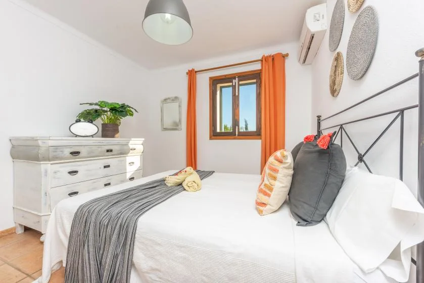 Un dormitorio luminoso con una cama, una cómoda blanca y cortinas naranjas.