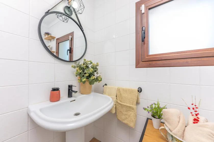 Un baño luminoso con lavabo, espejo redondo y ventana.