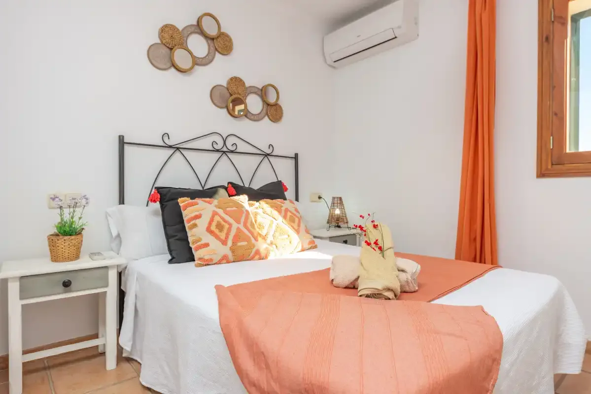 Un dormitorio con una cama bien arreglada, ropa de cama naranja y una ventana.