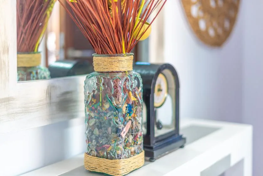 Un frasco decorativo de vidrio lleno de piezas coloridas está junto a un pequeño reloj.