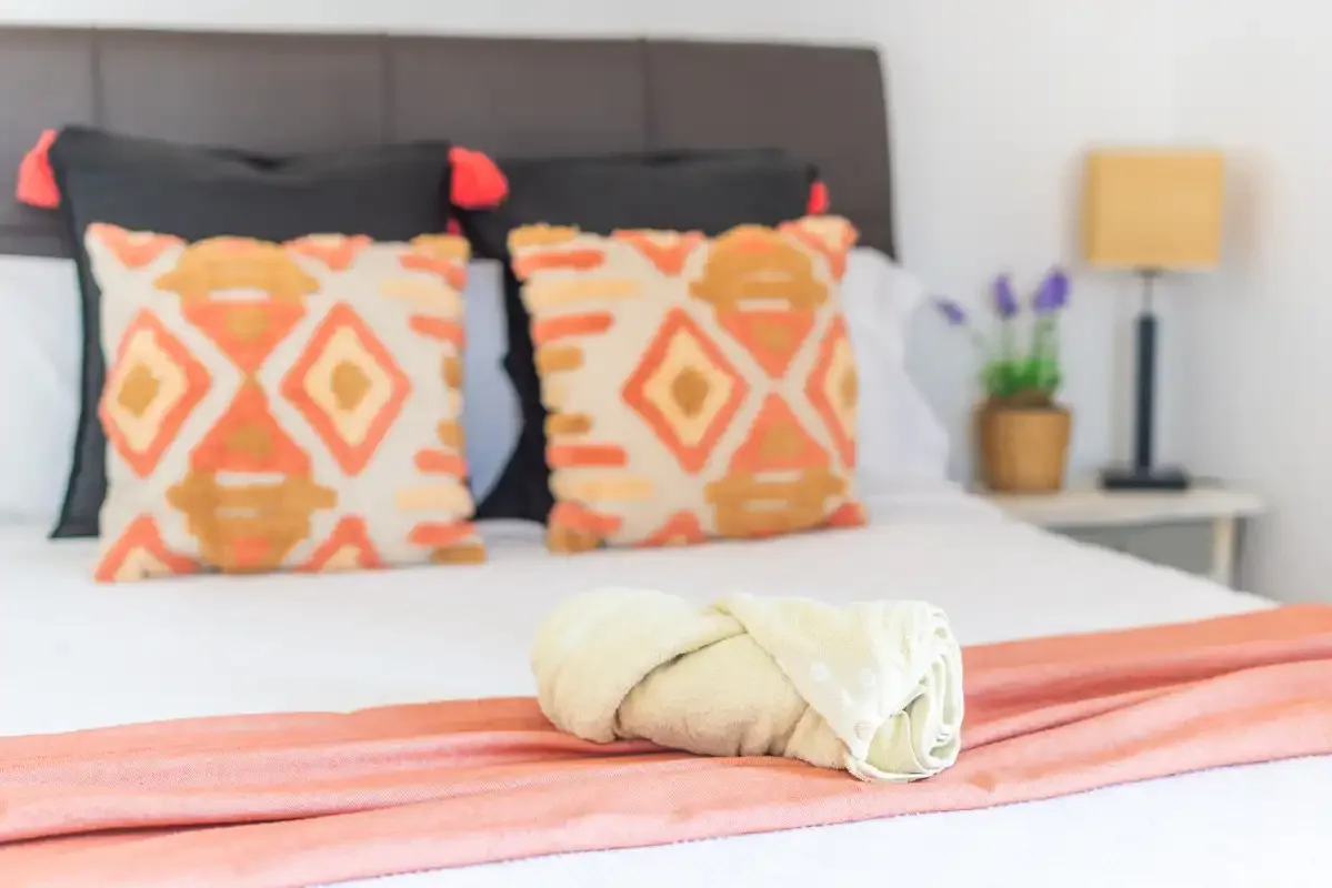 Dormitorio con cojines estampados y una toalla doblada sobre la cama.