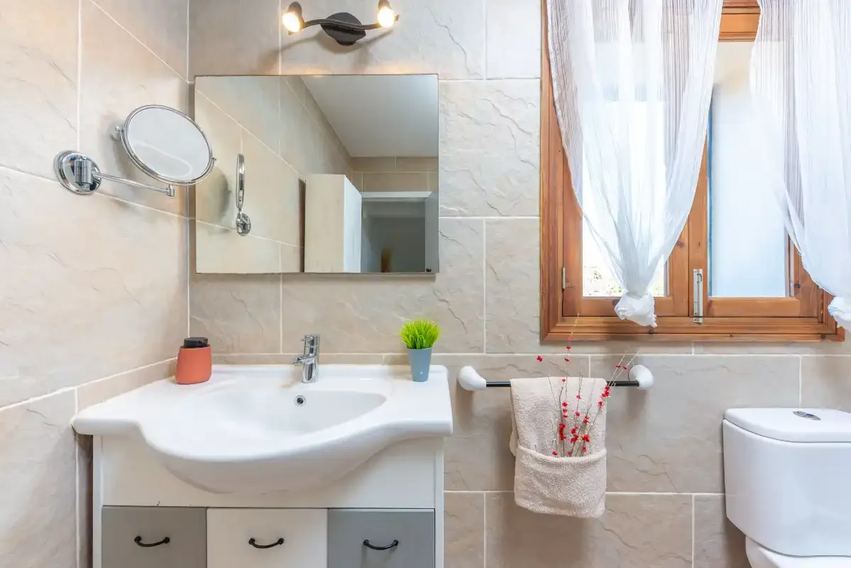 Un baño alicatado con lavabo, espejo y ventana con cortinas.
