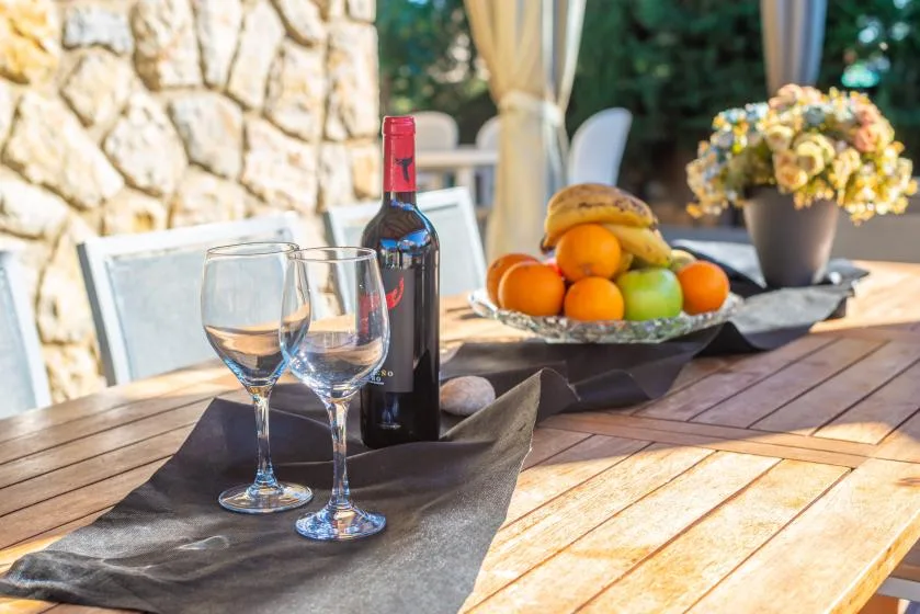 Una mesa de comedor al aire libre tiene copas de vino, una botella y un frutero.