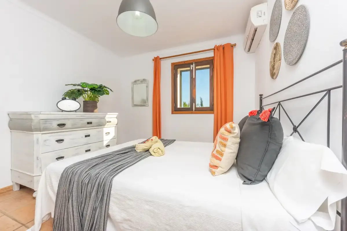 Un dormitorio luminoso con una cama, una cómoda blanca y cortinas naranjas.