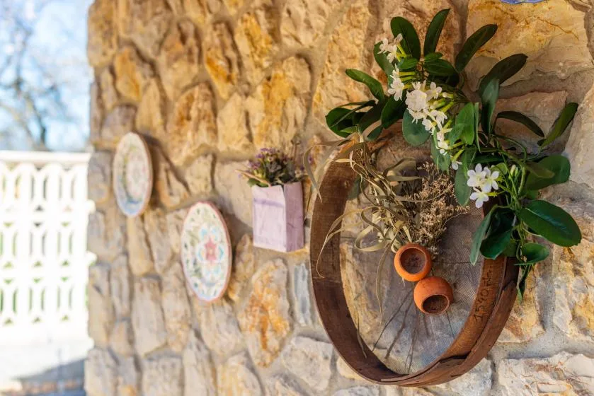 Una pared de piedra exhibe una jardinera circular de madera decorada con flores y follaje.