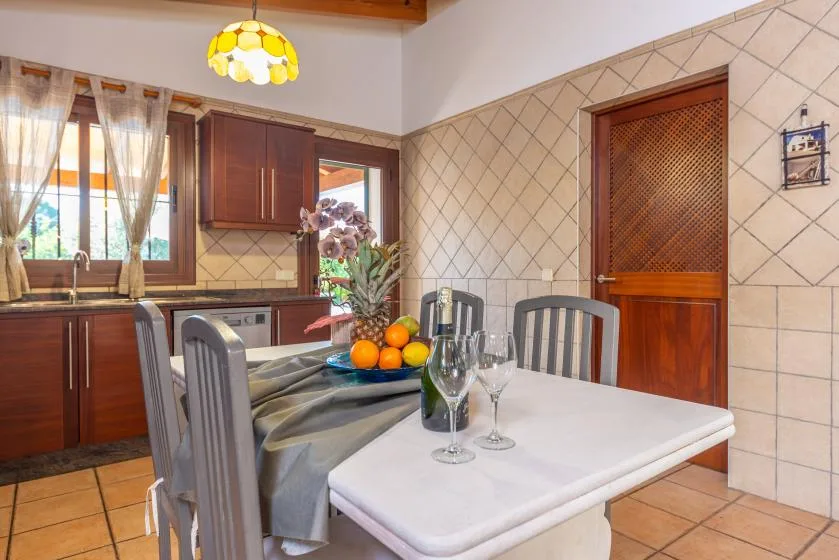 Un comedor con la mesa puesta está junto a una cocina con azulejos.