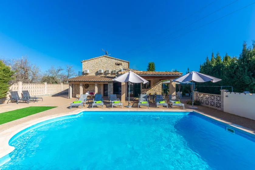 Una piscina ocupa el primer plano, con una casa de piedra y asientos en el patio detrás.