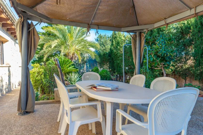 Un comedor exterior cubierto con una mesa y sillas, rodeado de vegetación.