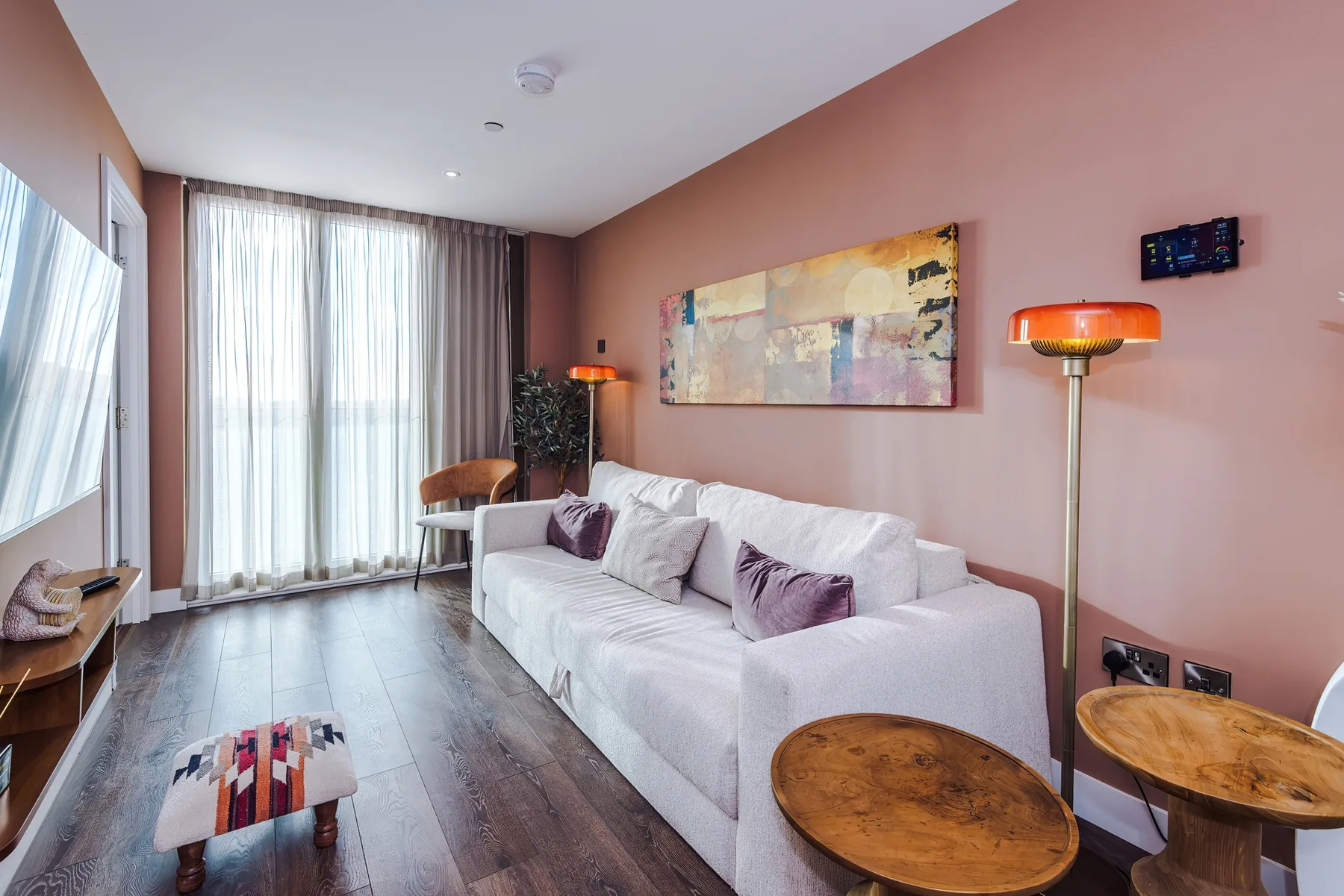 Sala de estar con un sofá blanco, arte colorido en la pared y cortinas largas.