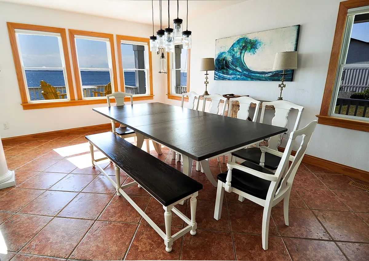 Comedor con una mesa larga, un banco y ventanas con vistas al mar.
