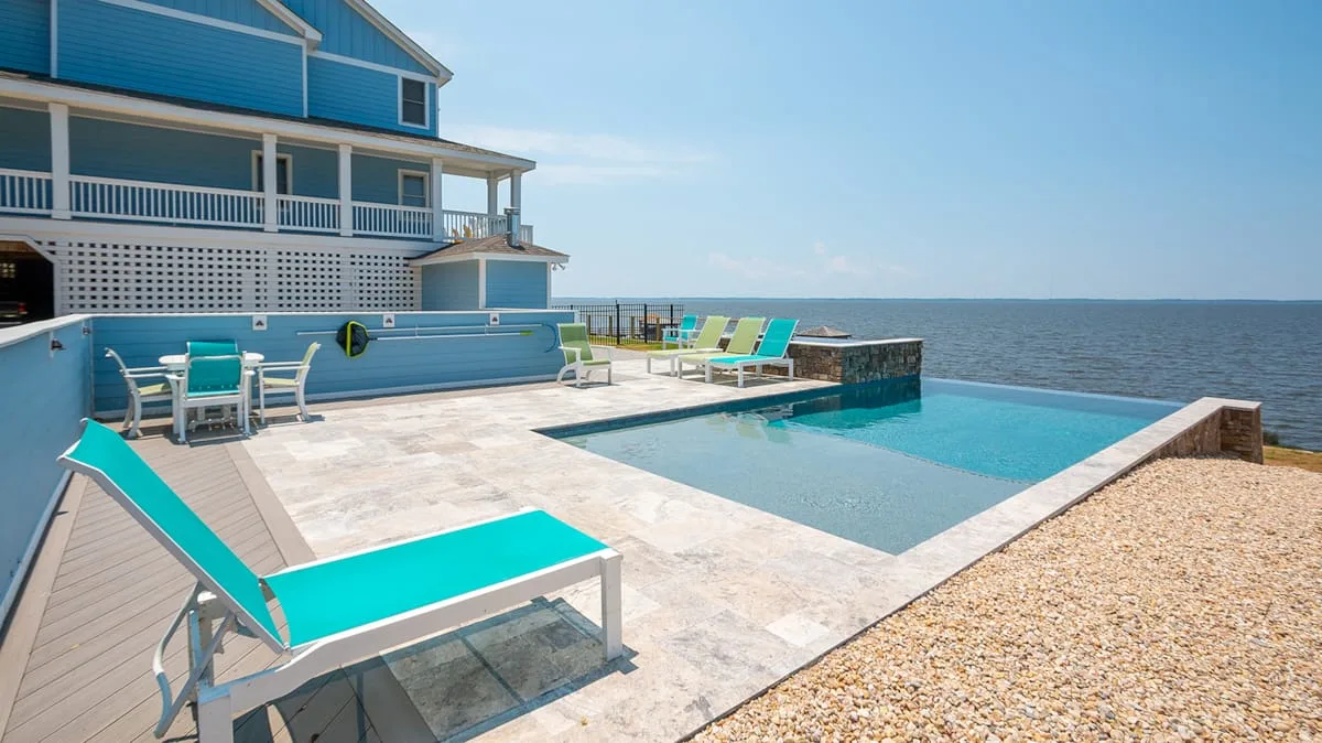 Una terraza con piscina junto a una casa frente al agua, con asientos orientados hacia la costa.