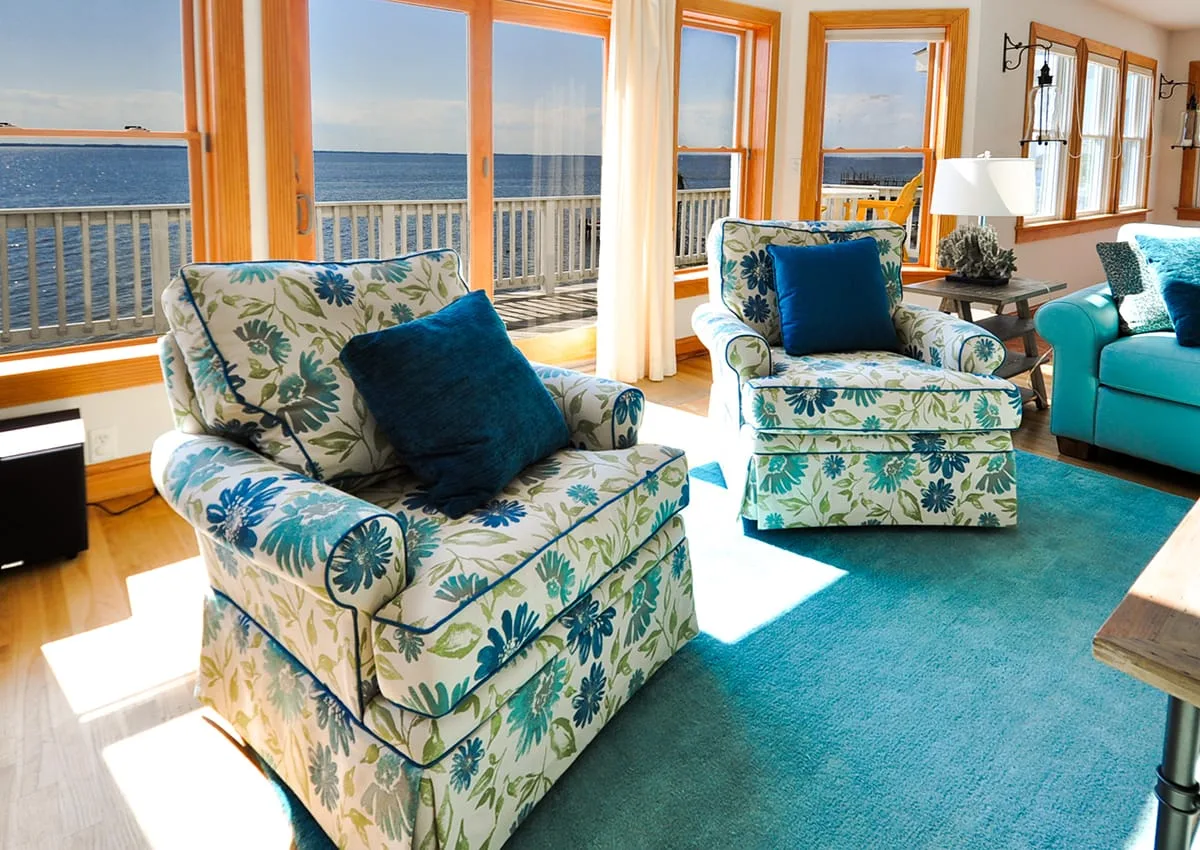 Una sala luminosa con asientos estampados junto a grandes ventanas con vista al agua.
