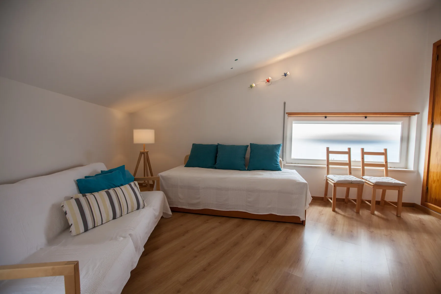 Un dormitorio luminoso con una cama, un sofá y una pequeña mesa de comedor junto a la ventana.