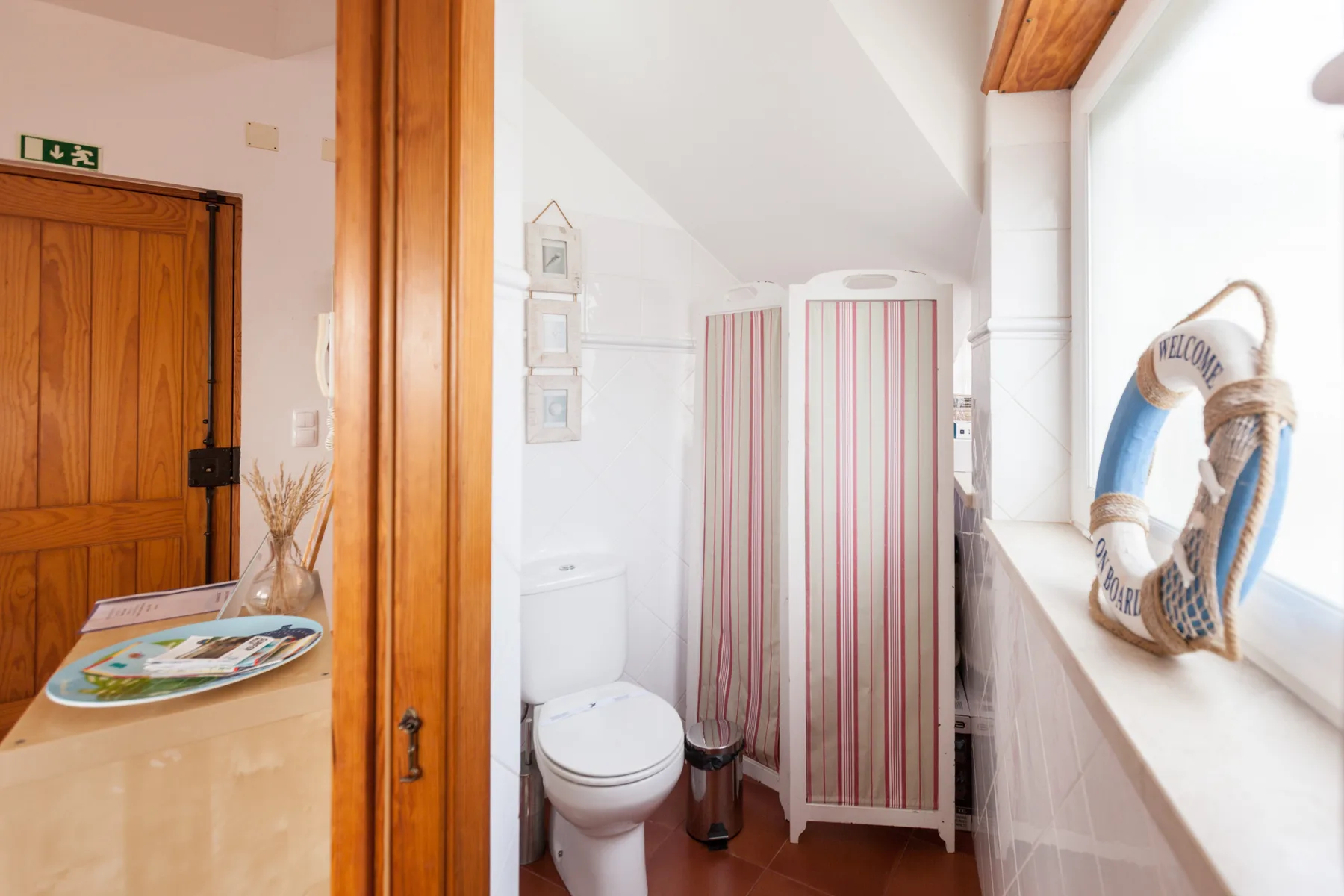 Un baño con inodoro, lavabo y cortina de ducha a rayas junto a una ventana.