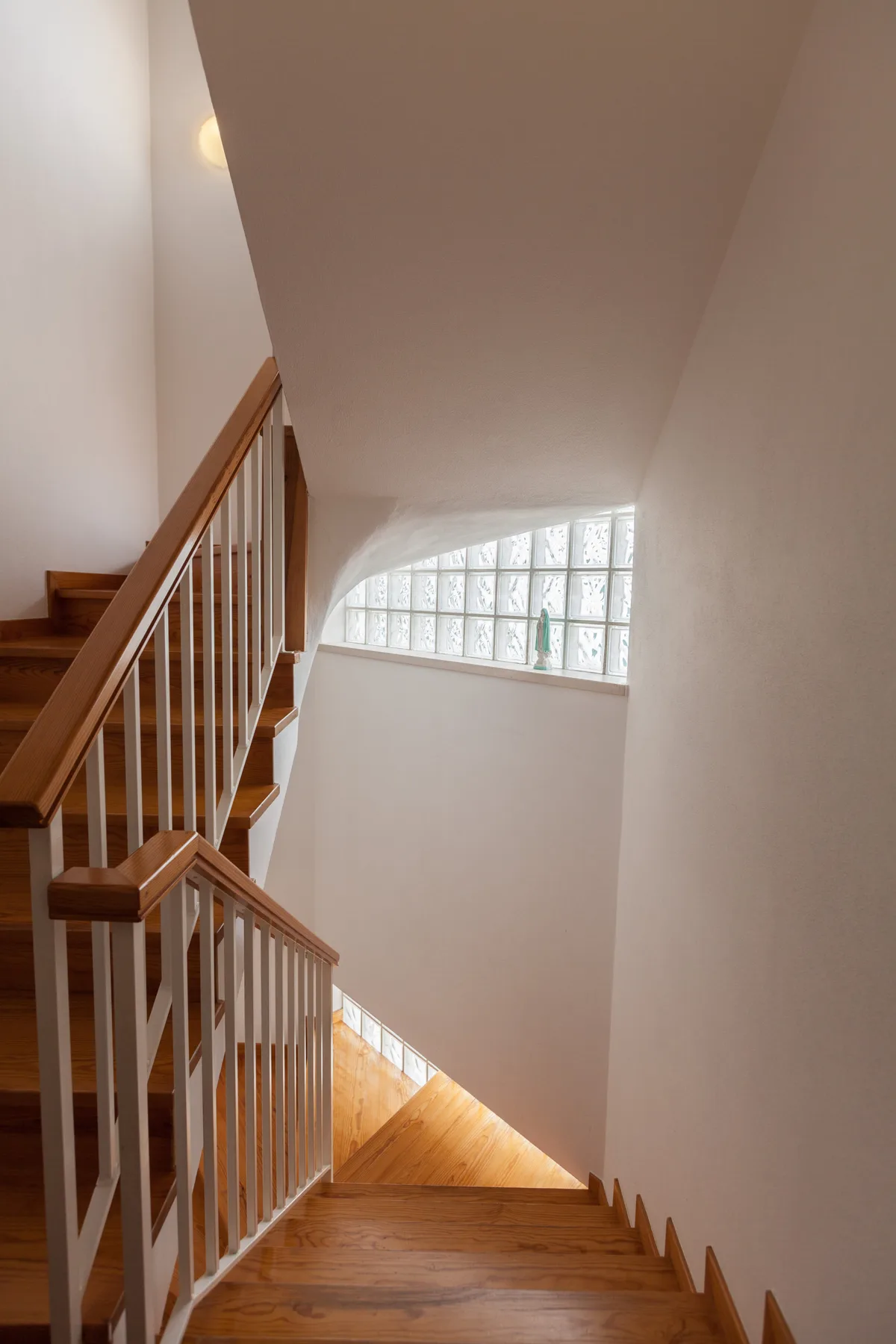 Una escalera con peldaños y barandillas de madera desciende junto a una ventana de bloques de vidrio.
