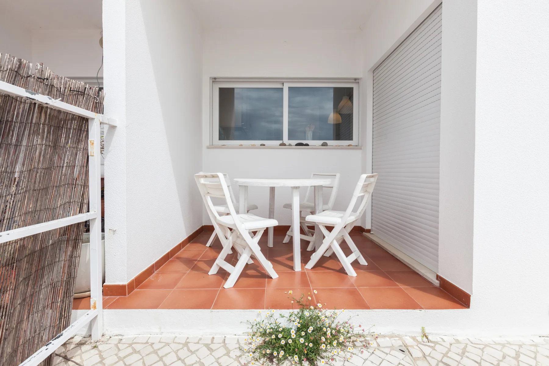 A small outdoor dining area with white seating and a table beside a window.