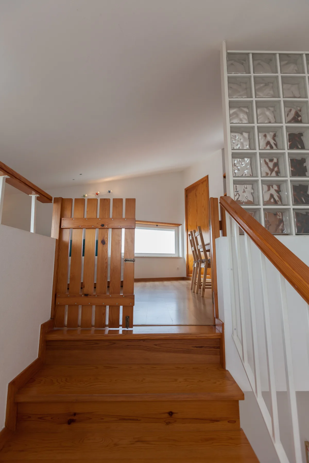 Una escalera de madera sube hacia un rellano junto a una pared de bloques de vidrio.