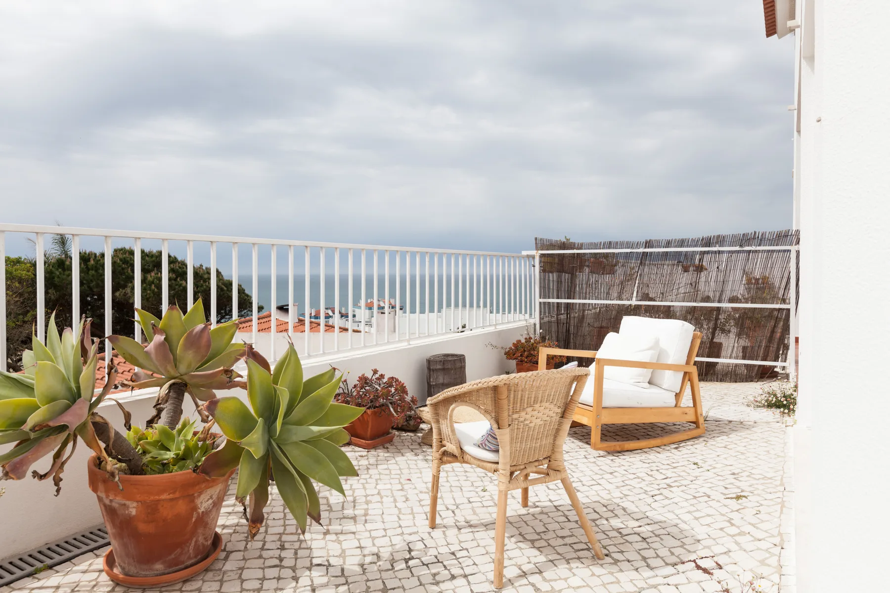 Una terraza embaldosada con asientos de mimbre, plantas en macetas y vistas al mar.