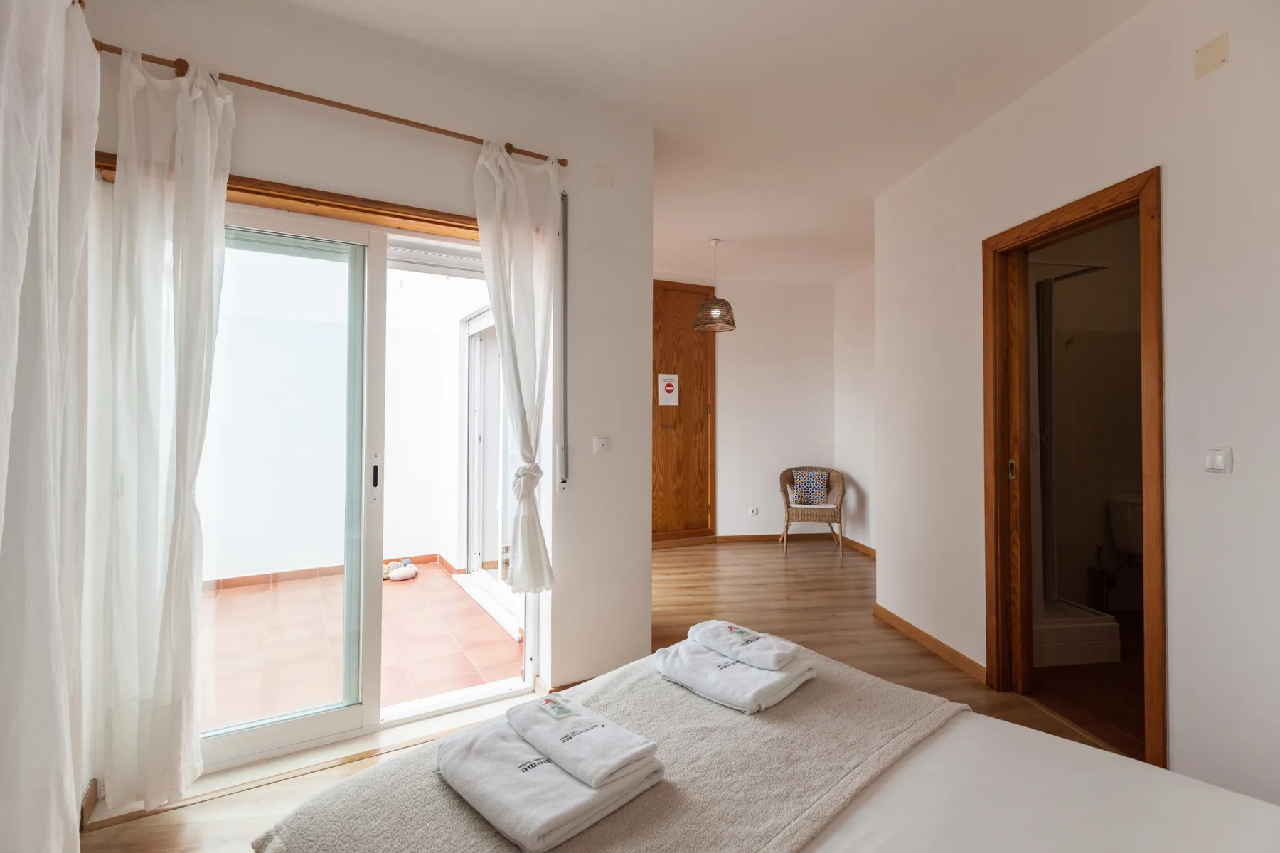 Un dormitorio con toallas dobladas sobre la cama junto a una puerta corrediza de vidrio.