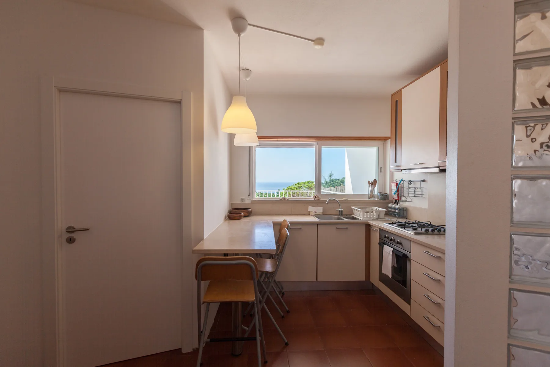 Una cocina compacta tiene armarios claros, una encimera y una ventana con vistas al mar.