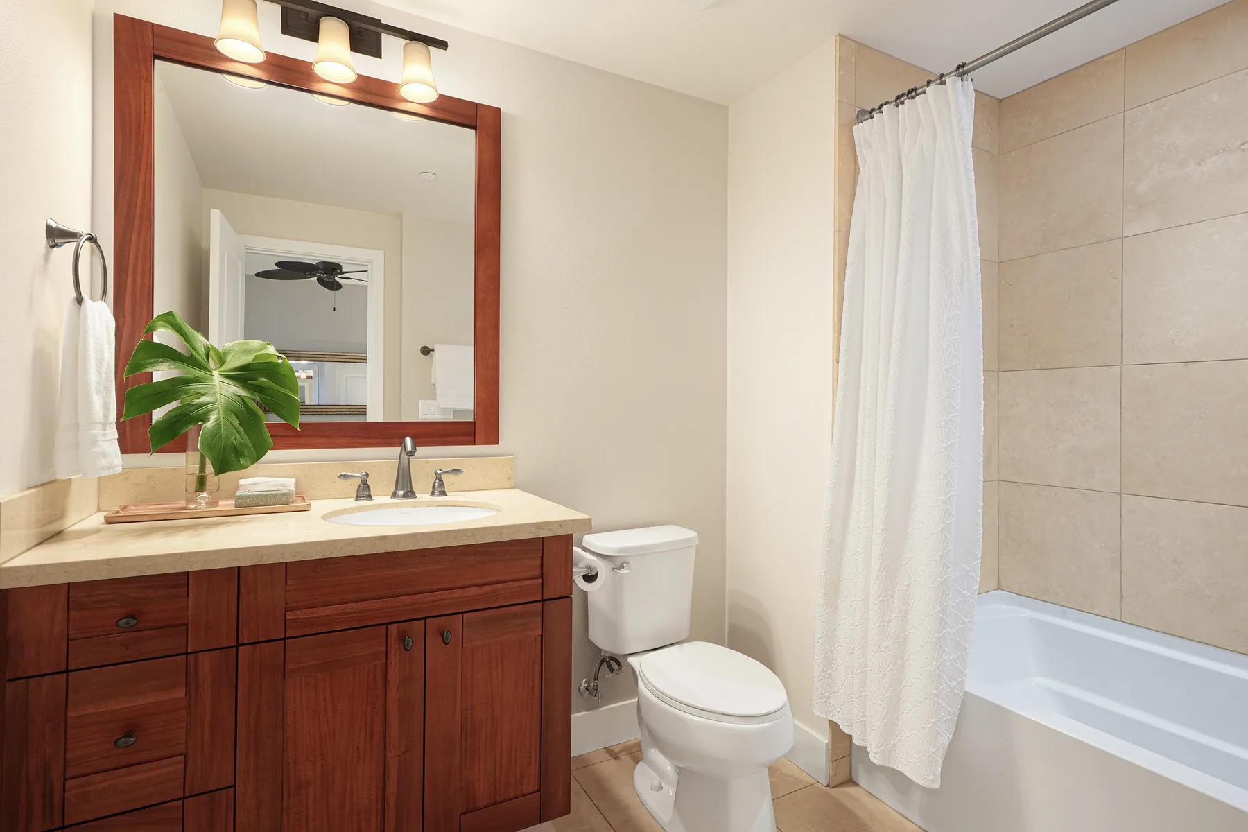 Un baño con mueble de madera, espejo, inodoro y bañera con cortina de ducha.