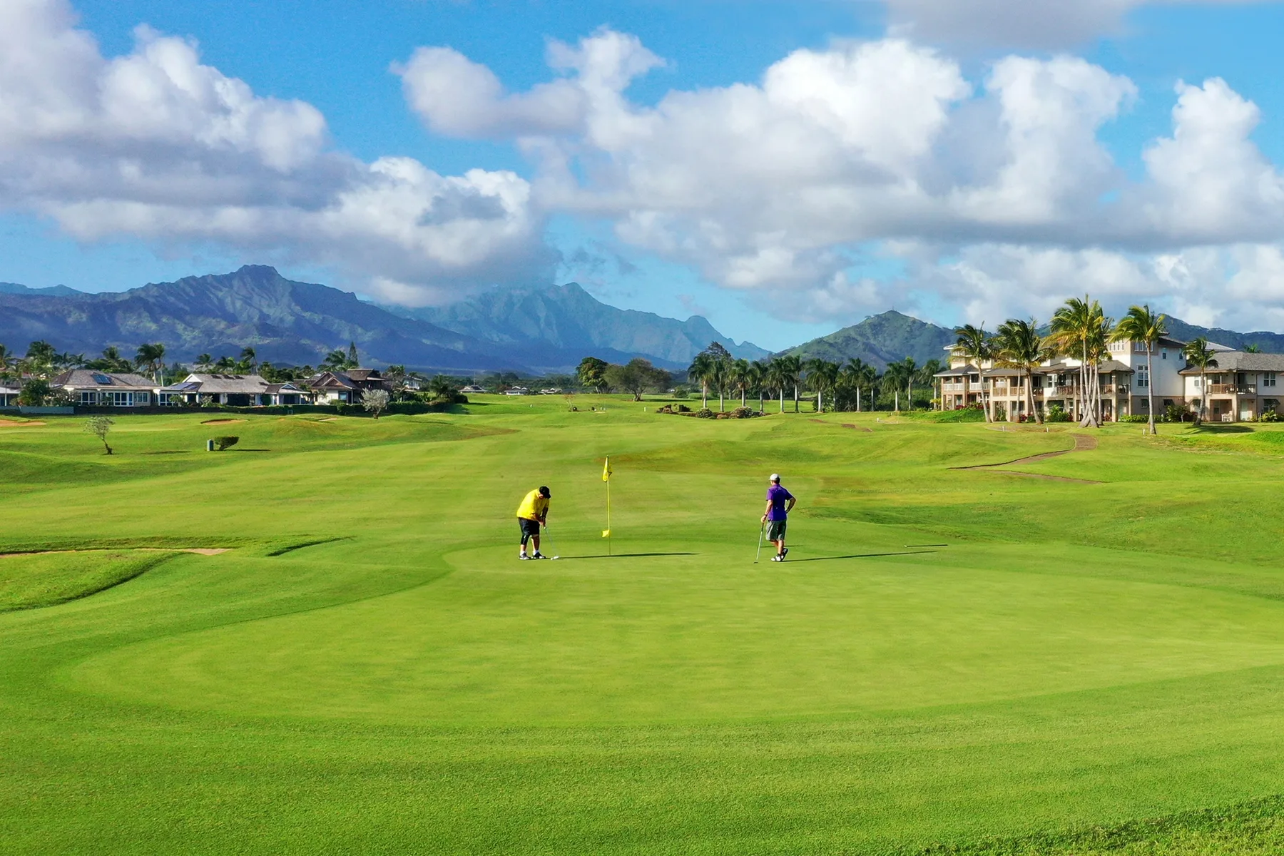 Un campo de golf se extiende por un paisaje verde con montañas a lo lejos.