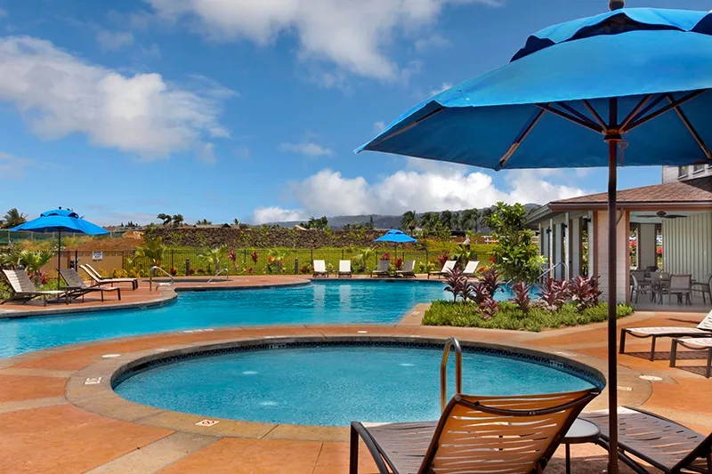 Zona de piscina al aire libre con una piscina circular más pequeña, sombrillas azules y asientos.