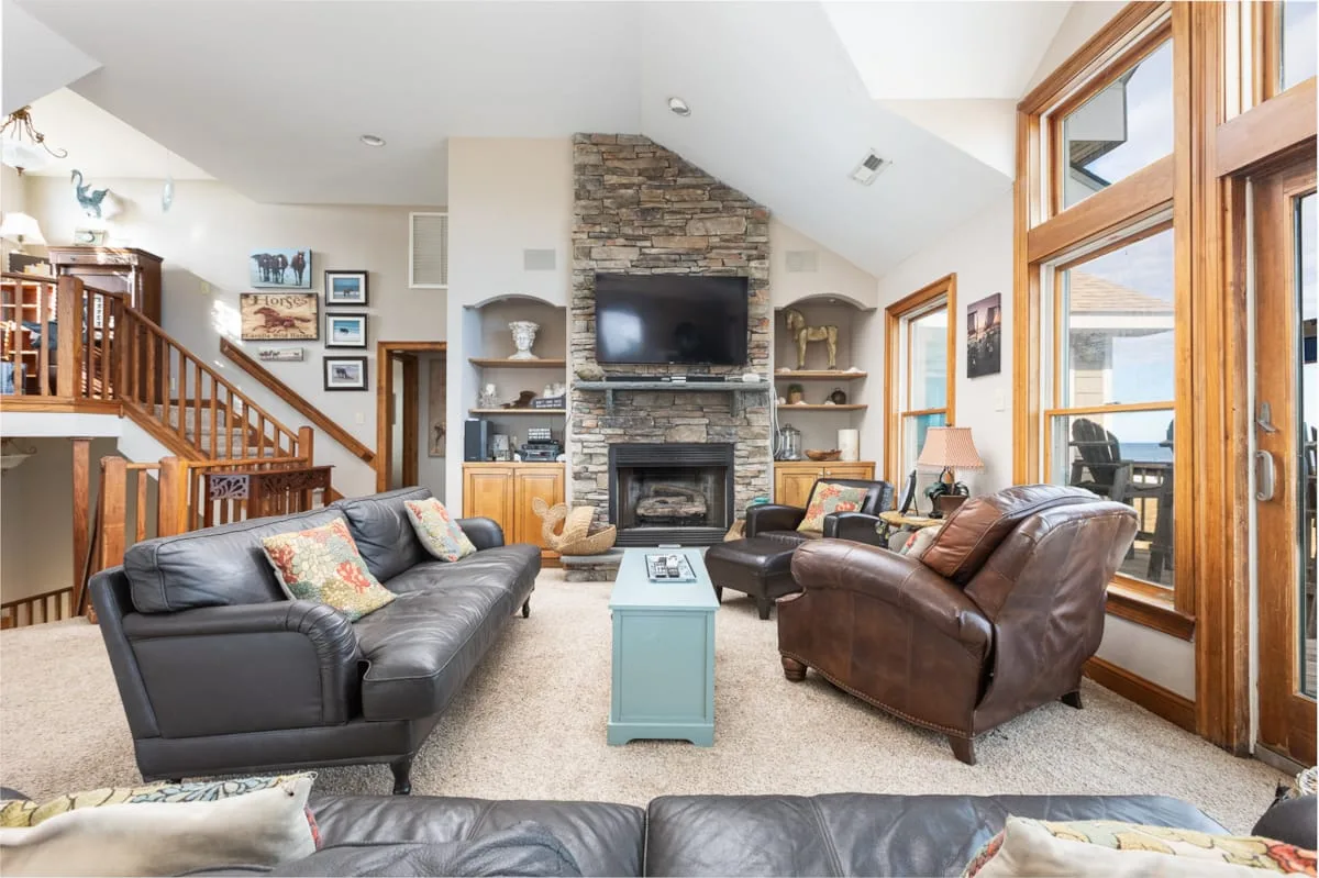 A living room with seating arranged around a stone fireplace and television.