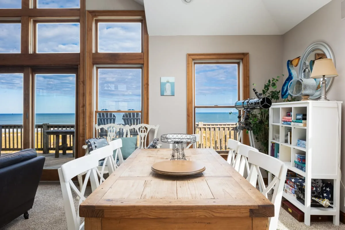 A dining area with a wooden table and large windows overlooking the water.