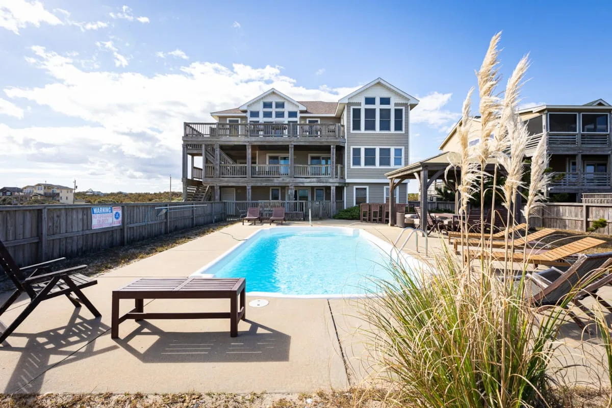 A swimming pool sits between multi-story buildings, with lounge seating around the deck.