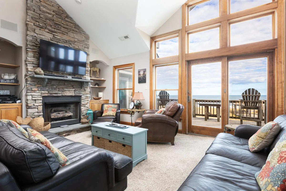 A bright living room with a stone fireplace and large windows overlooking the water.