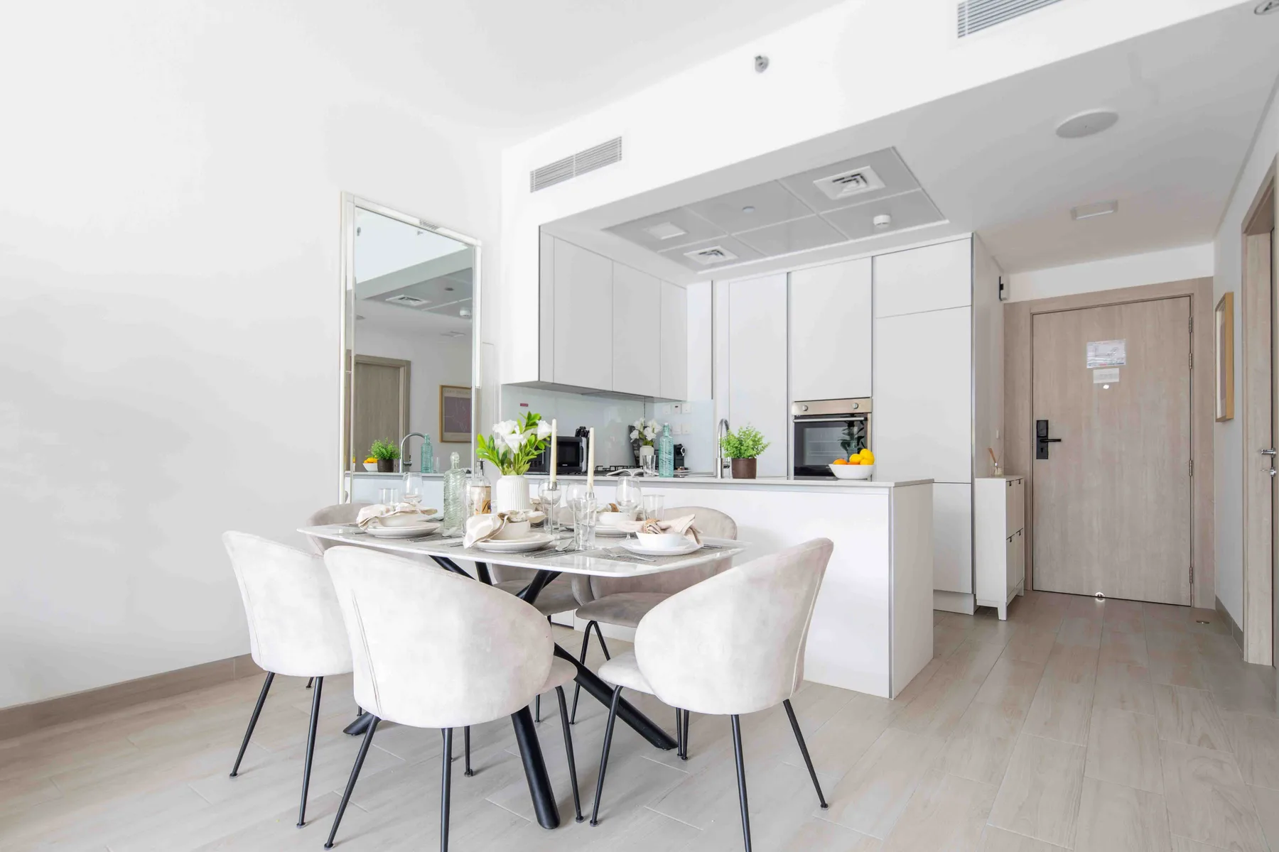 A bright dining area with a table and seating beside a white kitchen.