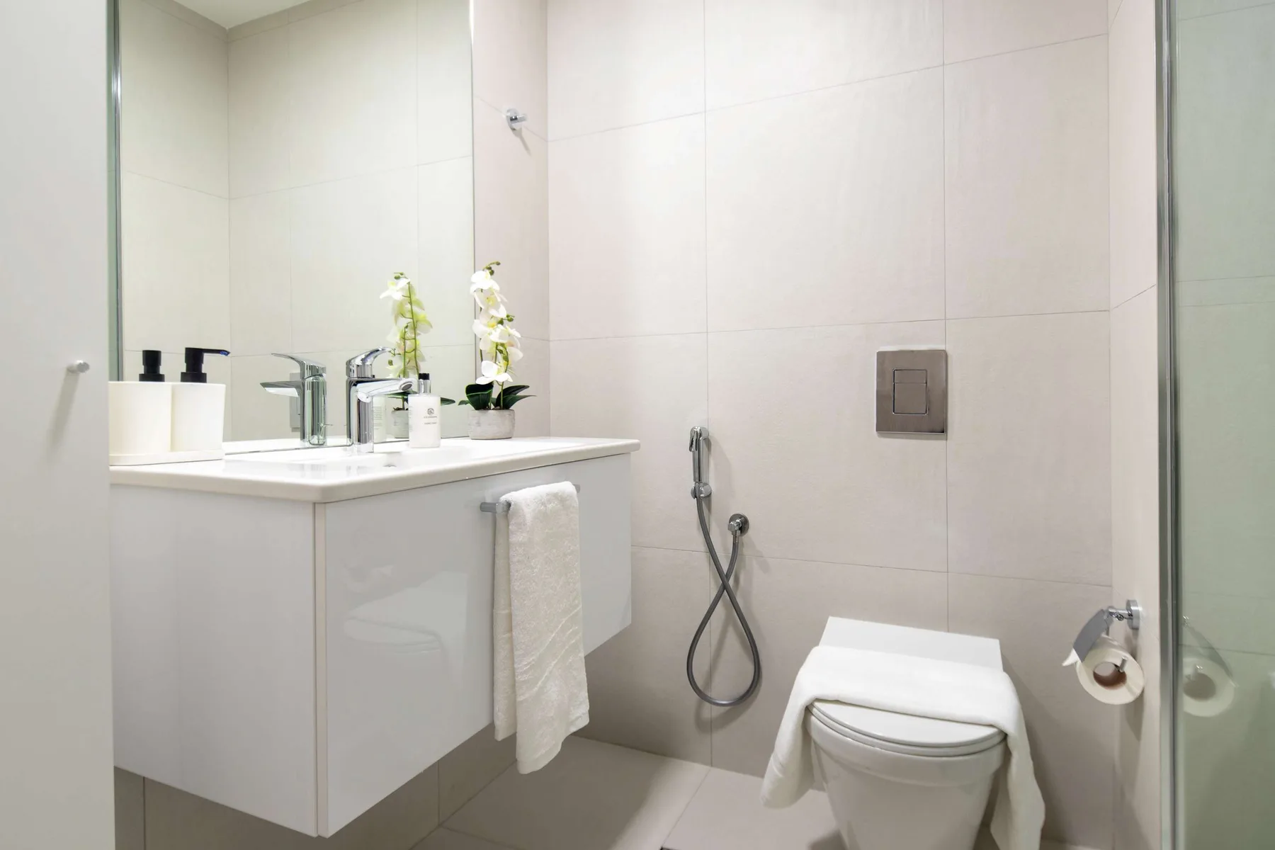 A bright bathroom with a sink, toilet, and wall-mounted shower fixtures.