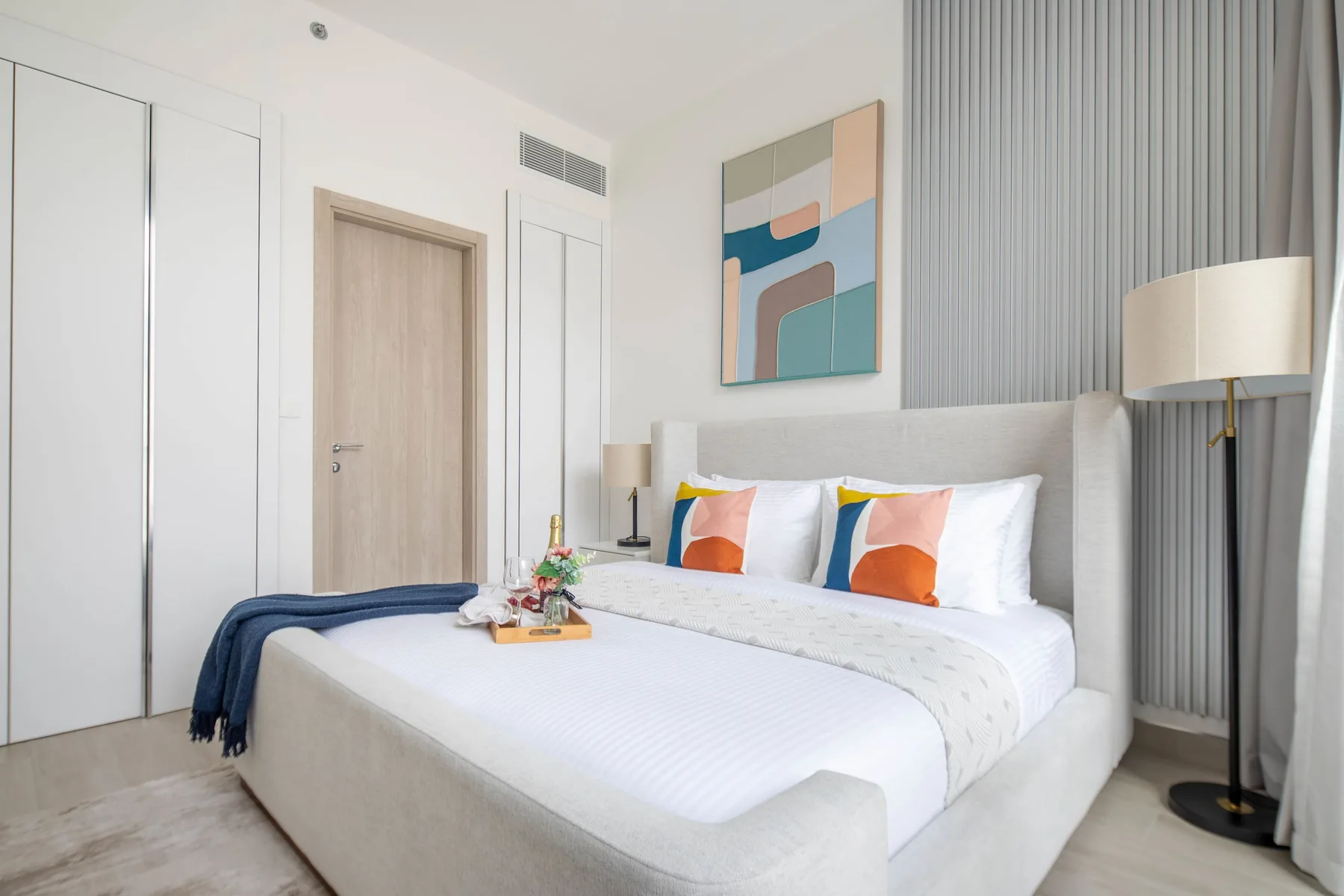 A bright bedroom with a neatly made bed and abstract wall art.