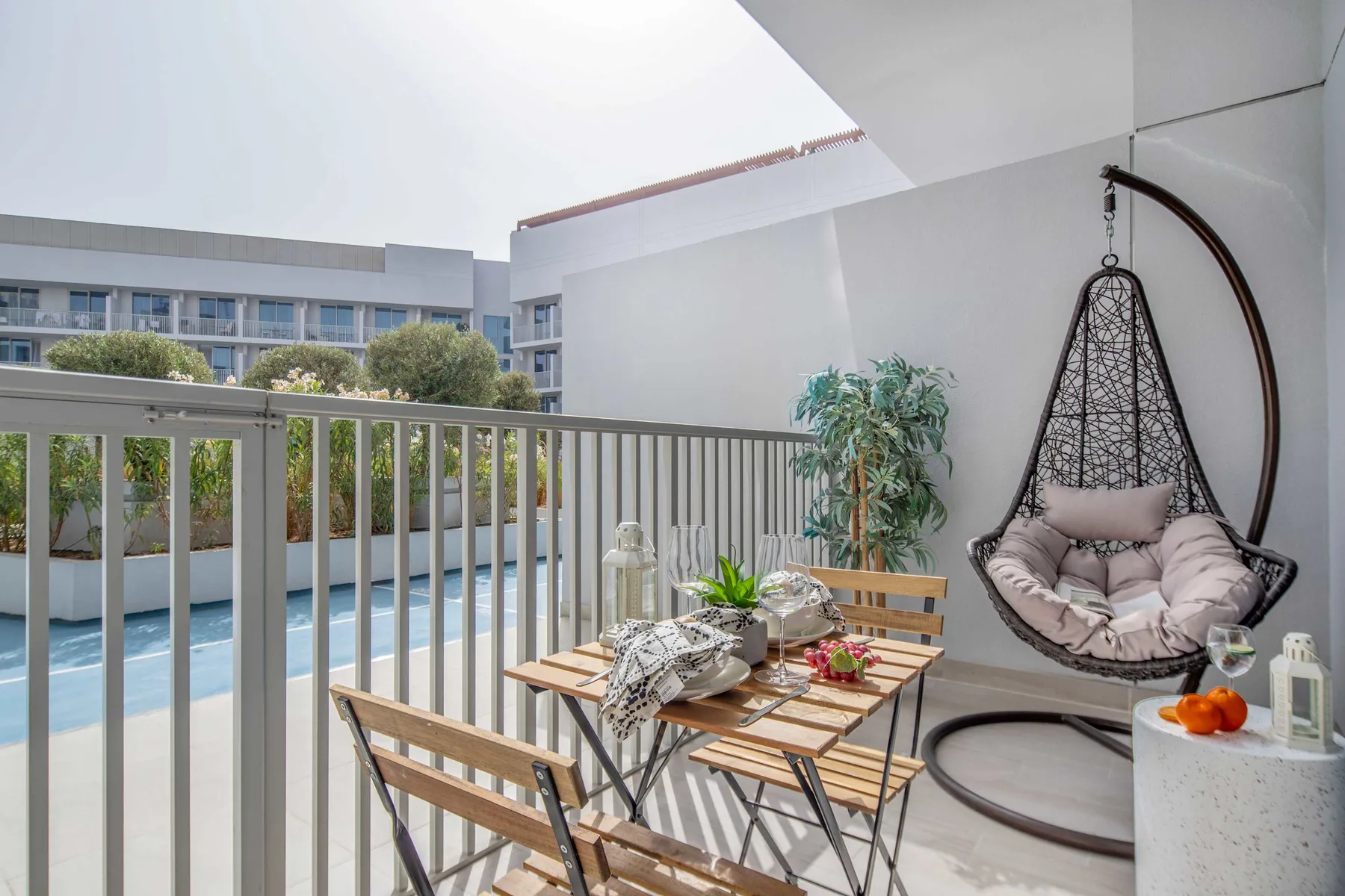 A furnished outdoor patio overlooks a swimming pool, with a hanging chair and table seating.