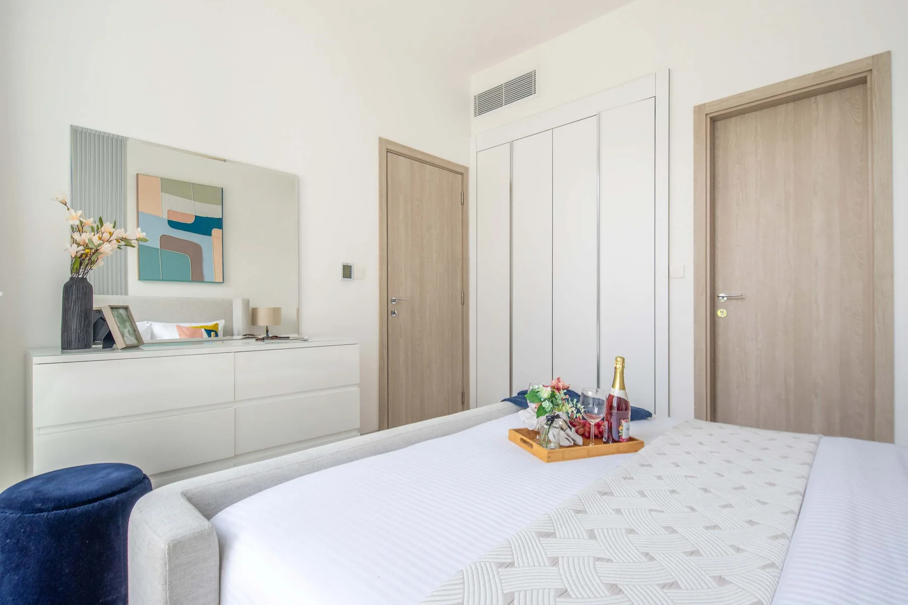 A bright bedroom with a bed, dresser, and built-in white cabinets.