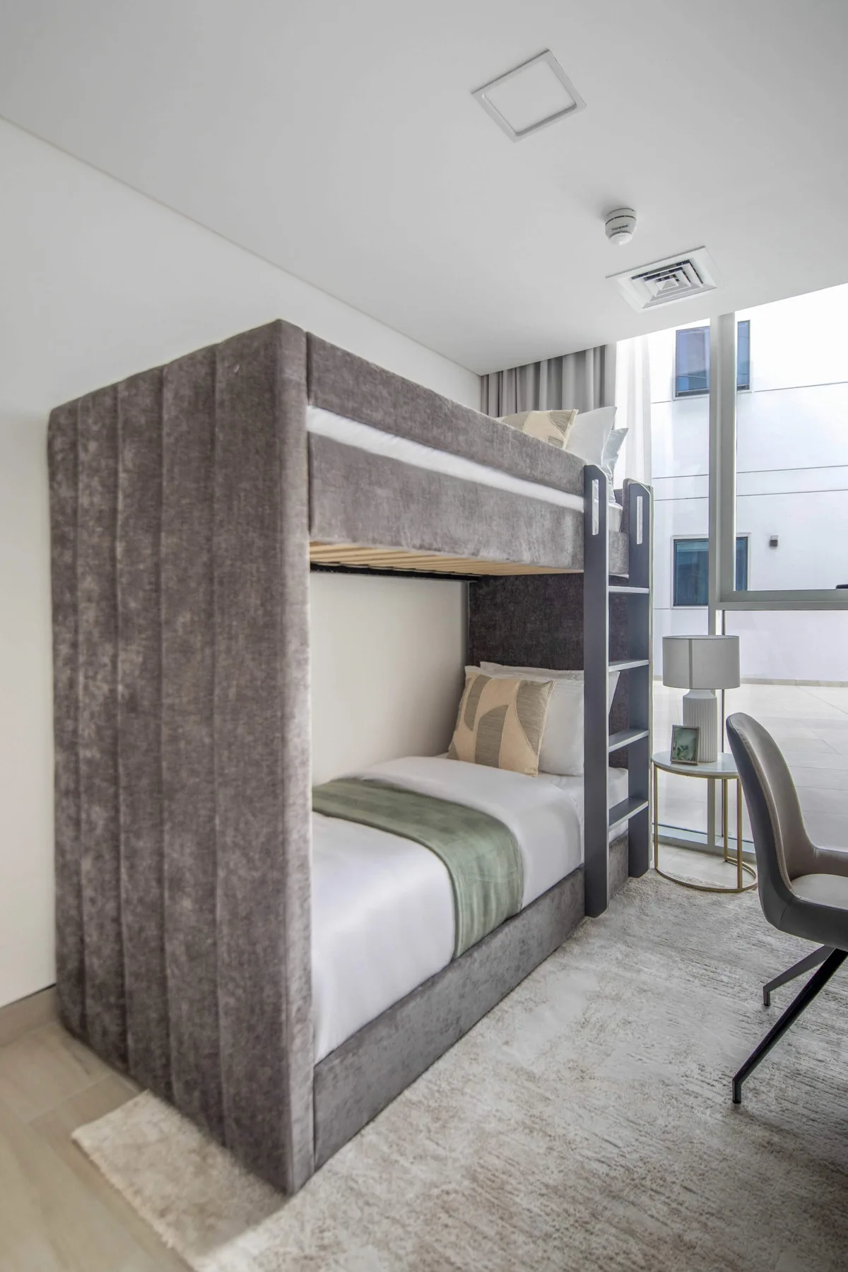 A bunk bed with gray fabric panels stands beside a large window.