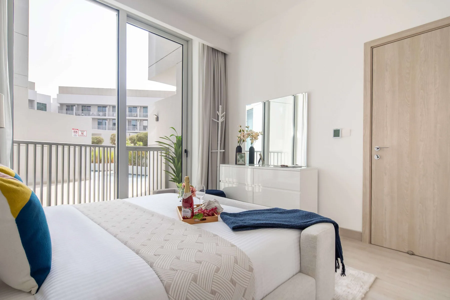A bright bedroom with a bed beside large windows and a dresser.