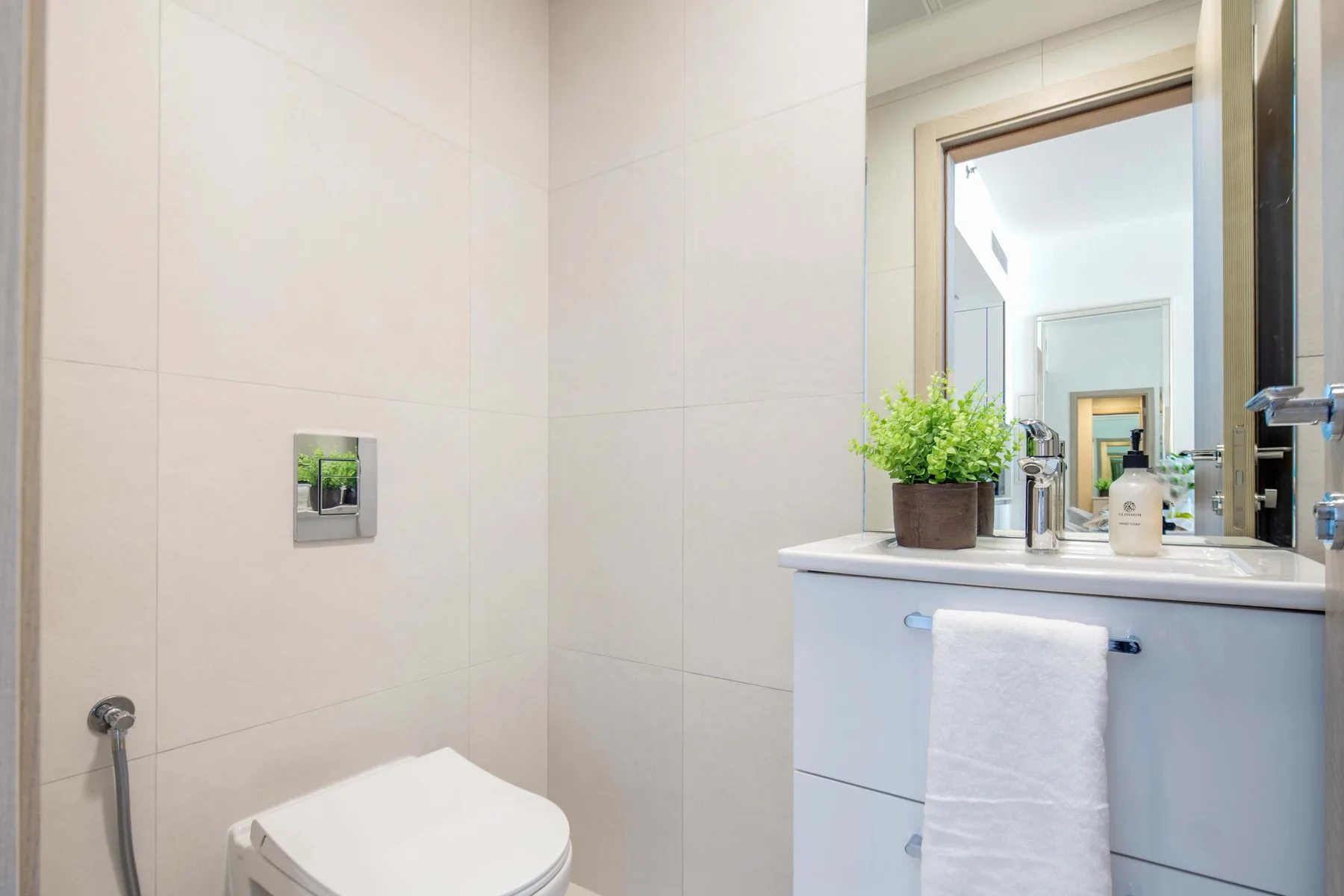 A tiled bathroom with a toilet and a sink vanity topped with a small plant.