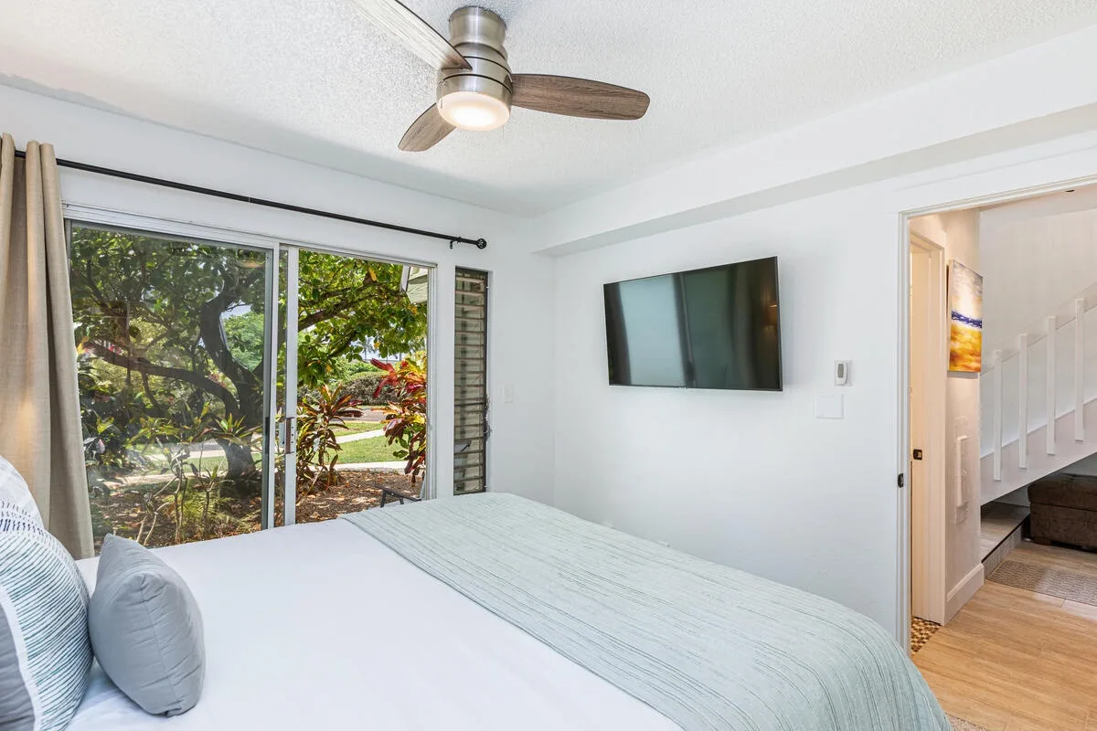 Un dormitorio luminoso tiene una cama junto a grandes ventanas con vista a árboles frondosos.