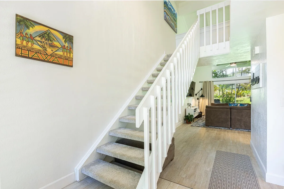 Una sala luminosa se abre junto a una escalera alfombrada con barandilla blanca.