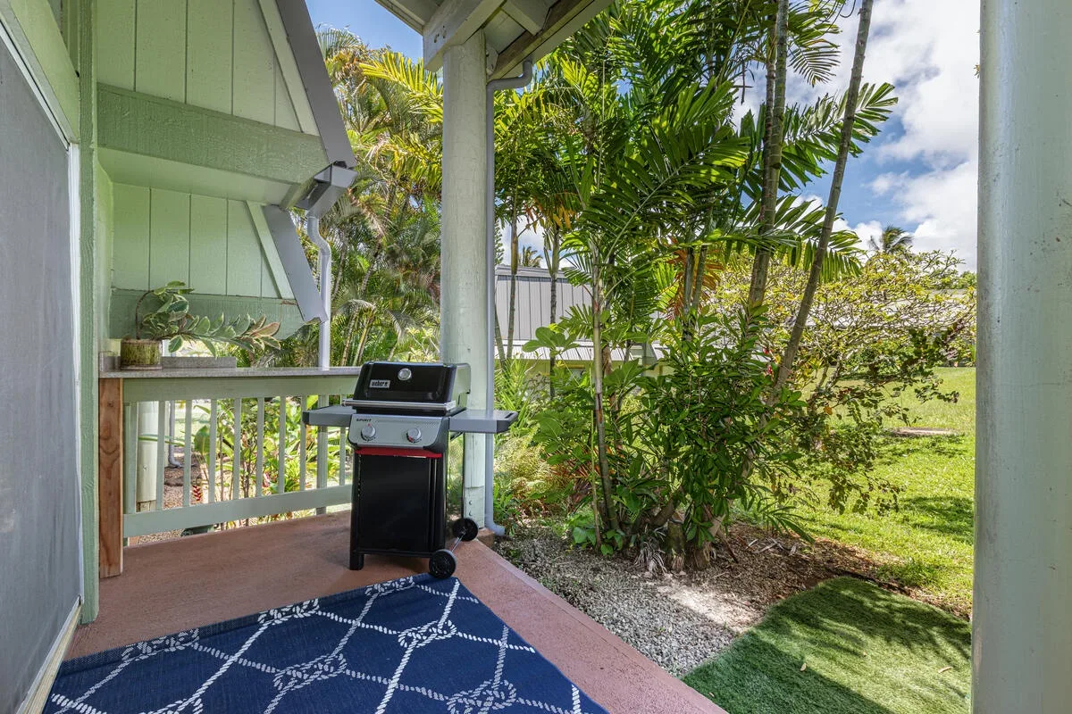 Un patio cubierto tiene una parrilla junto a plantas tropicales frondosas.