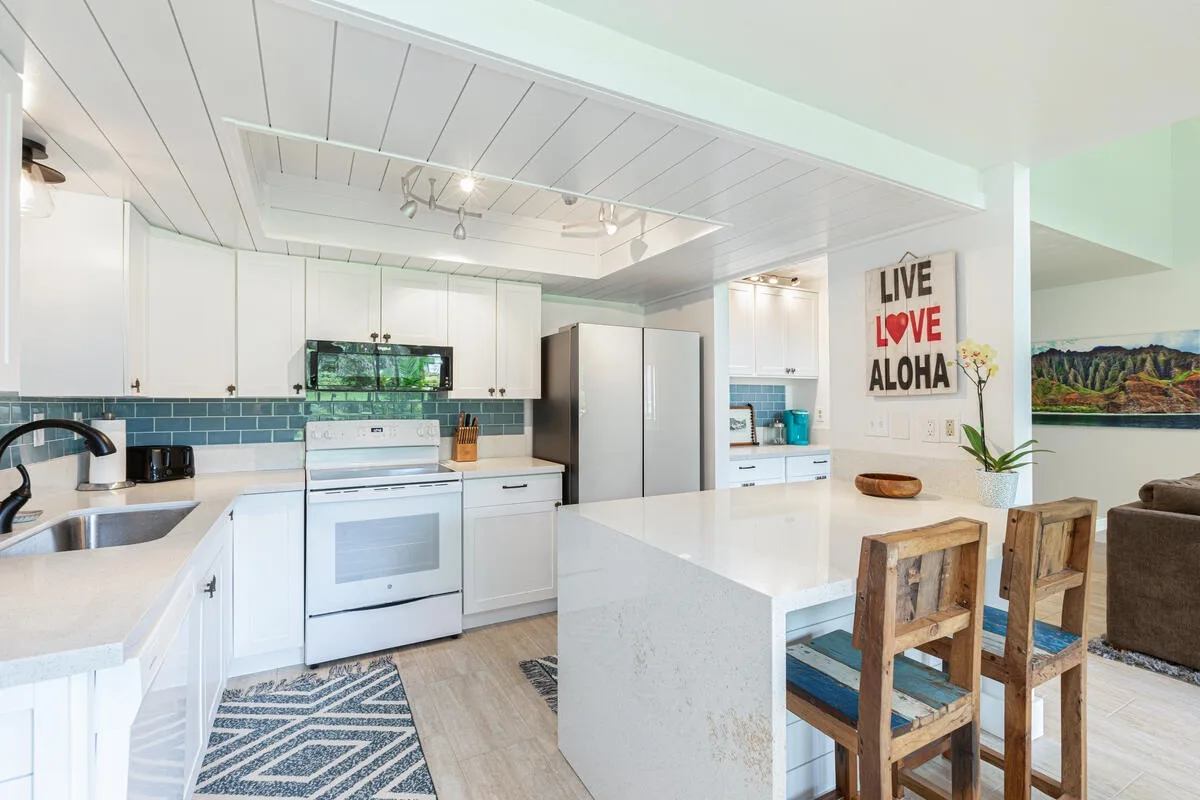 Una cocina luminosa con gabinetes blancos, una isla central y asientos de barra.