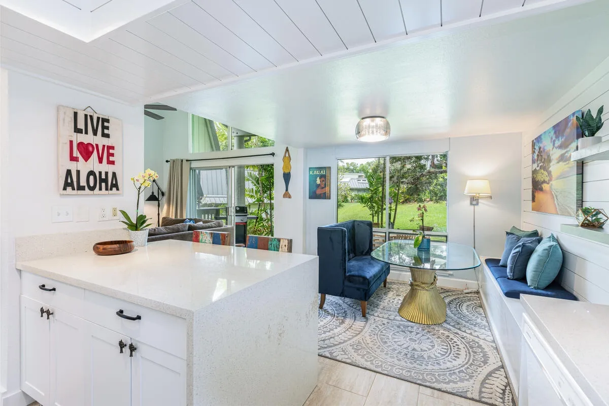 Una sala luminosa con una isla de cocina blanca, asientos y una mesa de centro de vidrio.