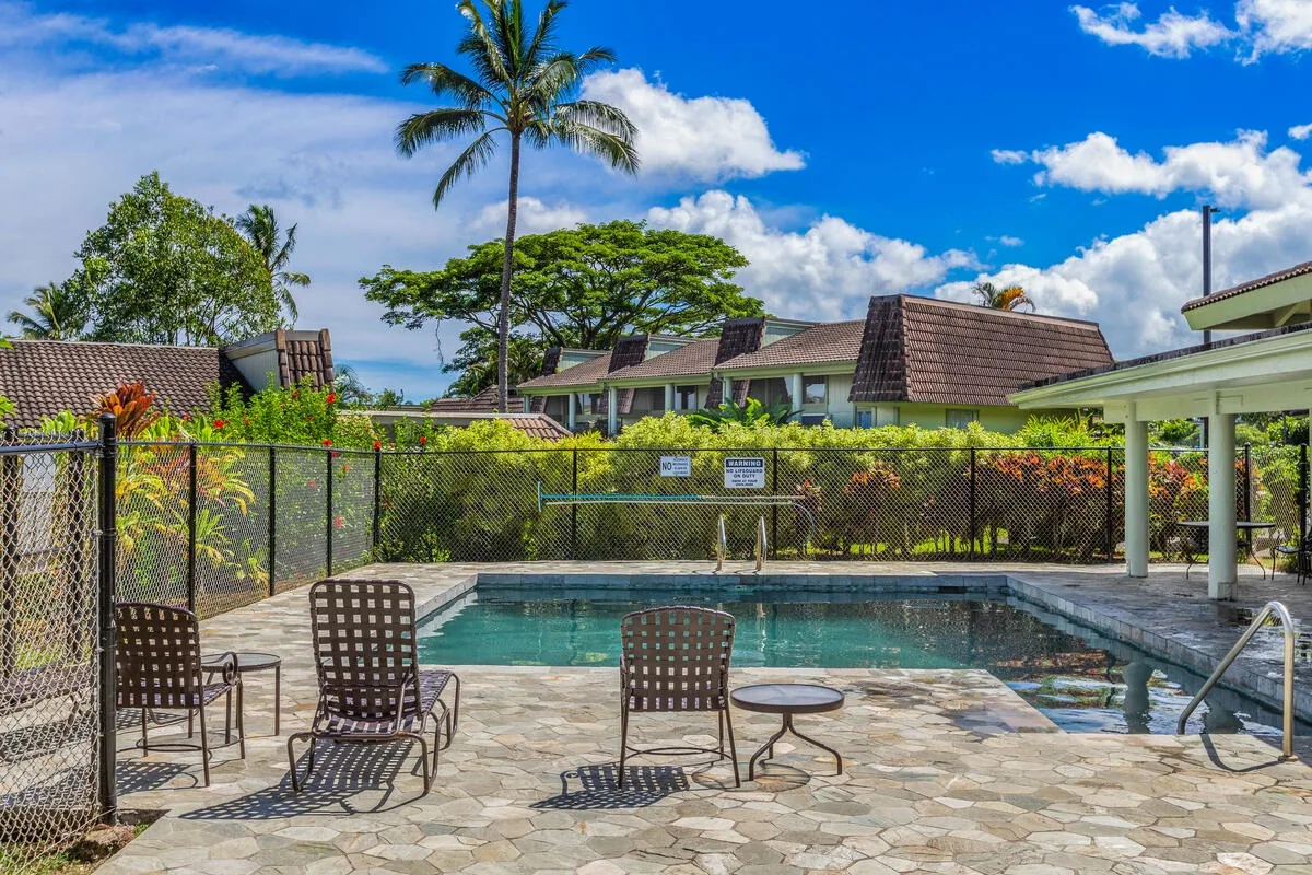 Una piscina al aire libre está rodeada de asientos de patio y vegetación tropical.